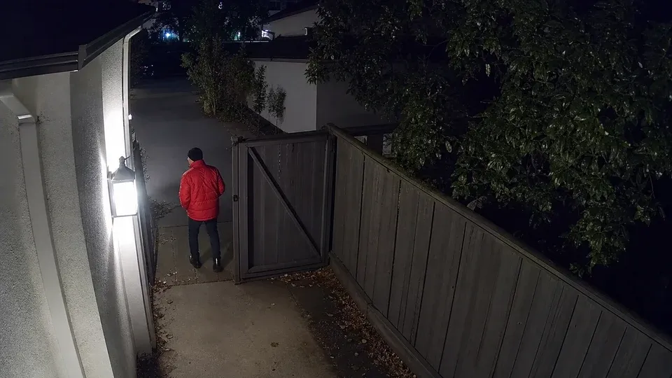person in red jacket near the side gate, after dark